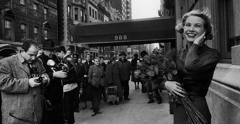 Actress Grace Kelly in casual pose with armful of roses standing on sidewalk